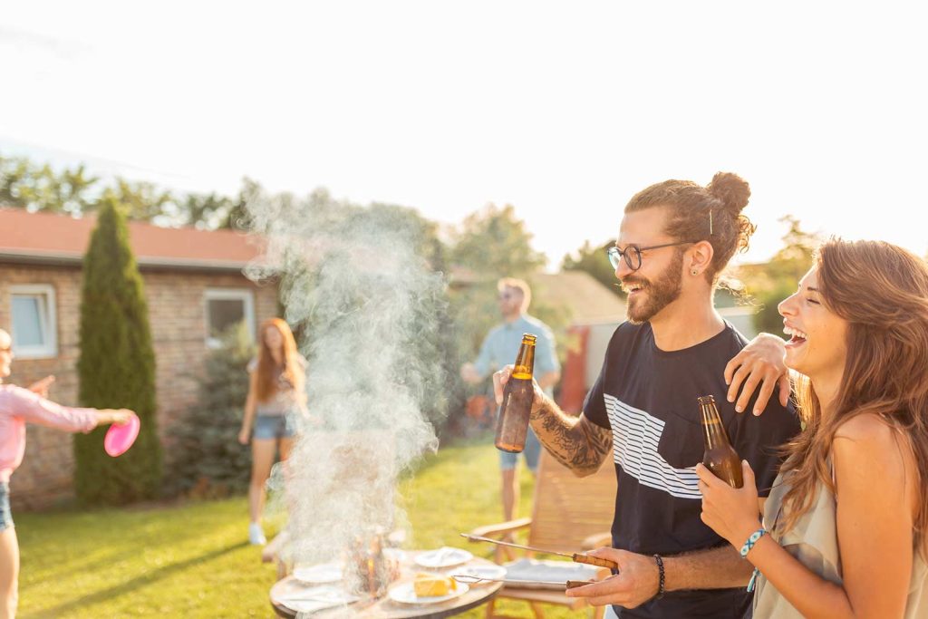 Friends drinking beer and playing frisbee at a backyard bbq picnic